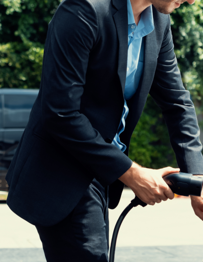 Closeup progressive black suit businessman insert EV charger plug from public charging station to his electric car. Eco friendly electric rechargeable car with zero CO2 emission.